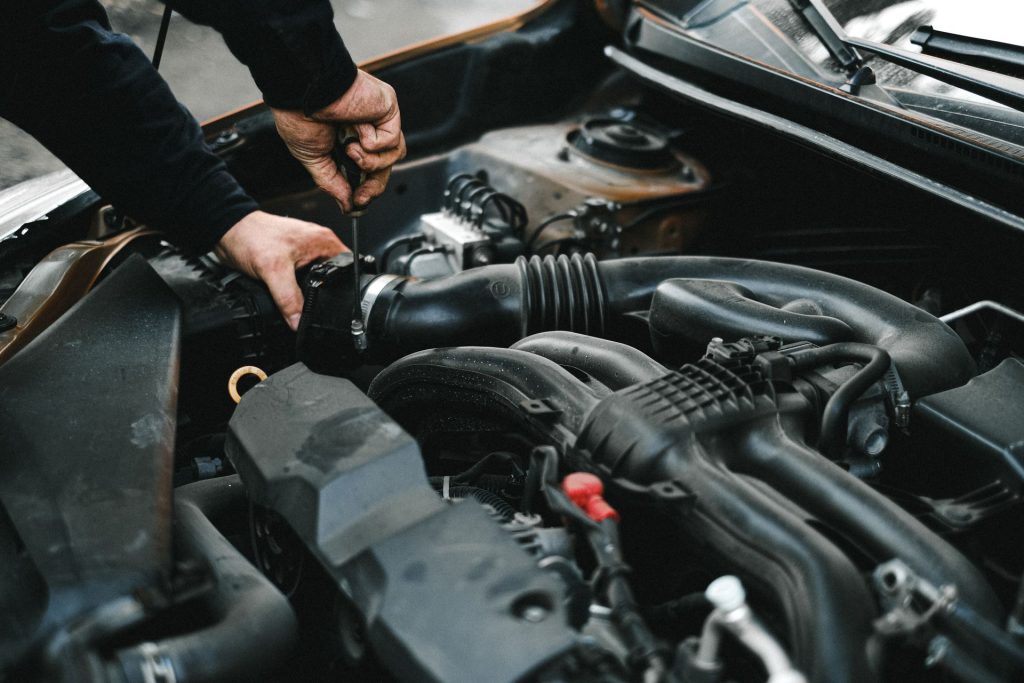 Hände arbeiten im geöffneten Motorraum eines Pkw