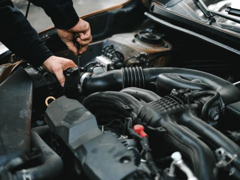 Hände arbeiten im geöffneten Motorraum eines Pkw