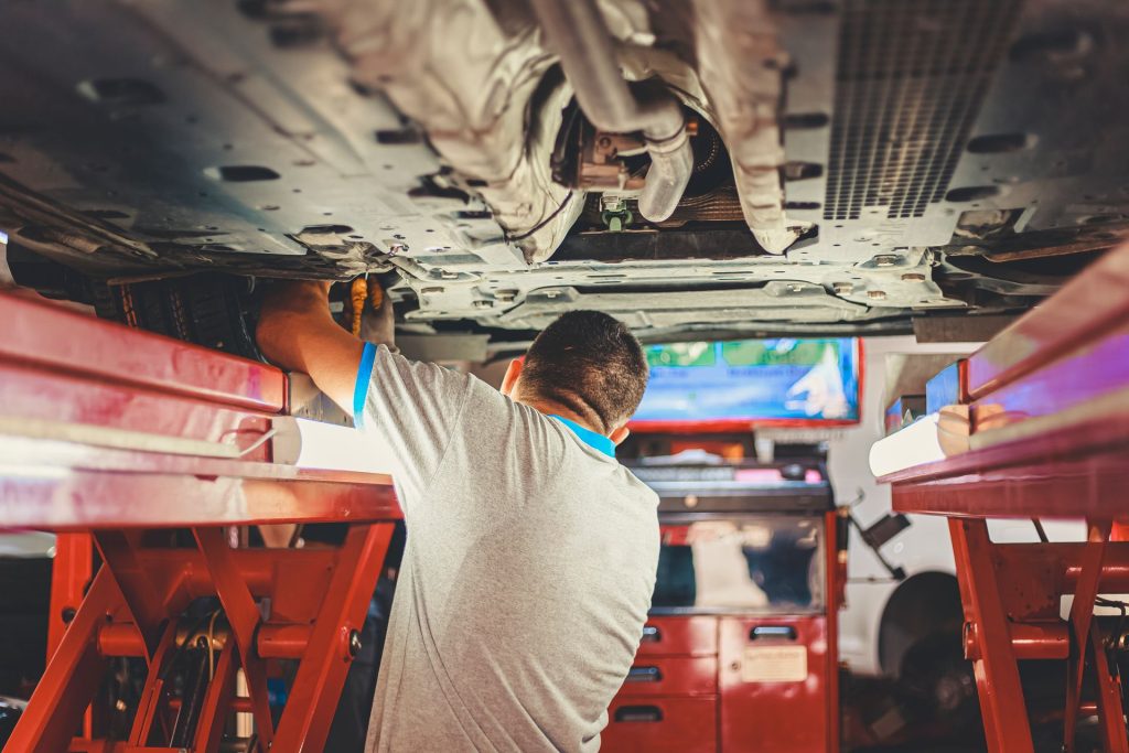 Mechaniker prüft die Unterseite eines Fahrzeugs auf der Hebebühne
