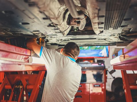 Mechaniker prüft die Unterseite eines Fahrzeugs auf der Hebebühne