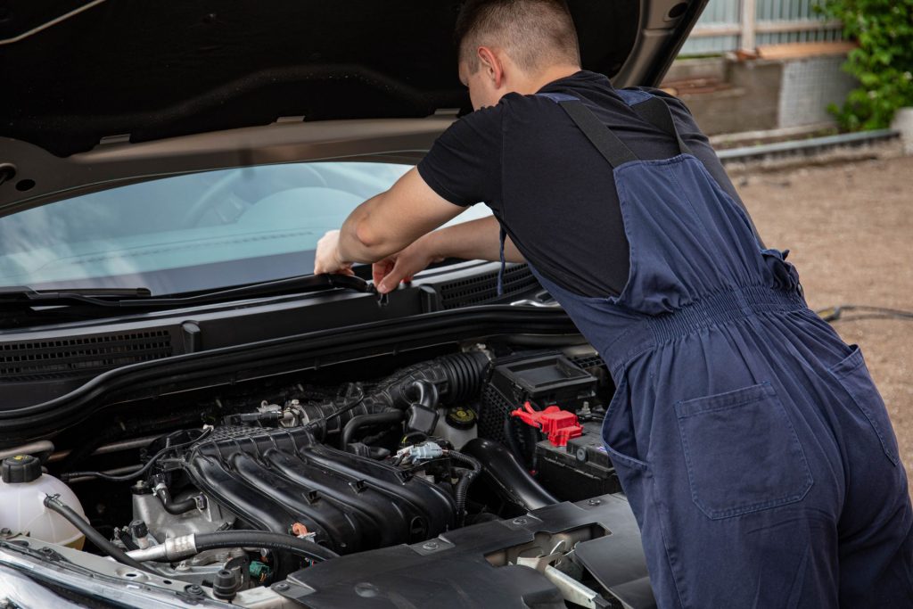 Mechaniker im Overall beugt sich über einen offenen Motorraum